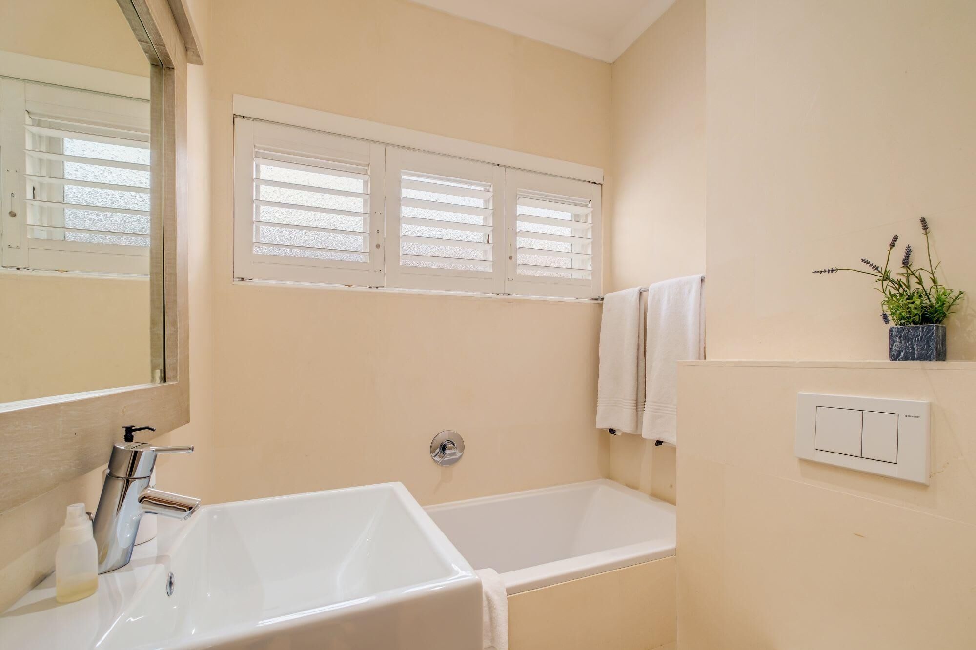 A bathroom with a white bathtub, a sink, and a window with blinds.