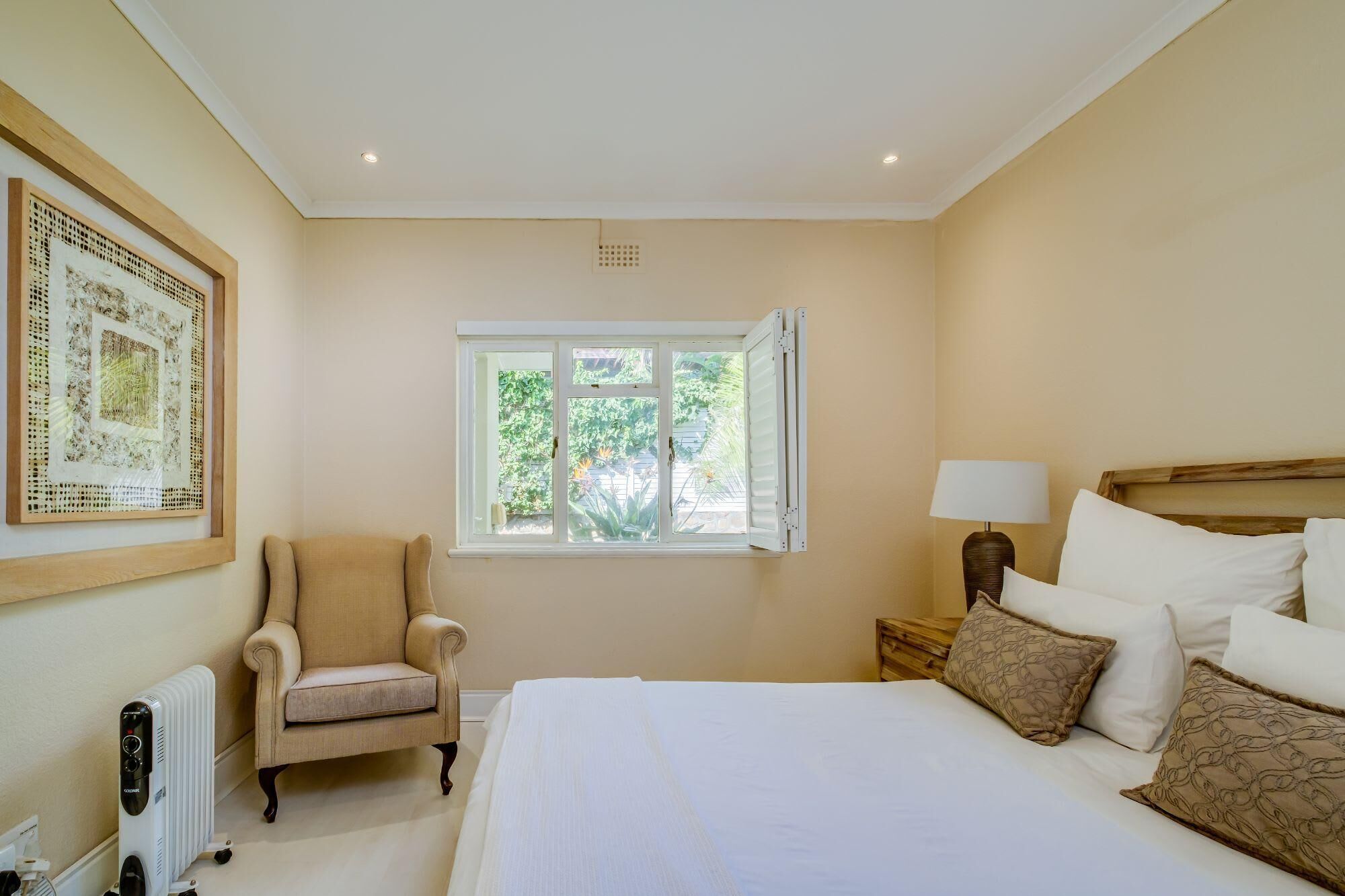 Un dormitorio con cama, una silla, una mesita de noche, una lámpara y una ventana con contraventanas abiertas.