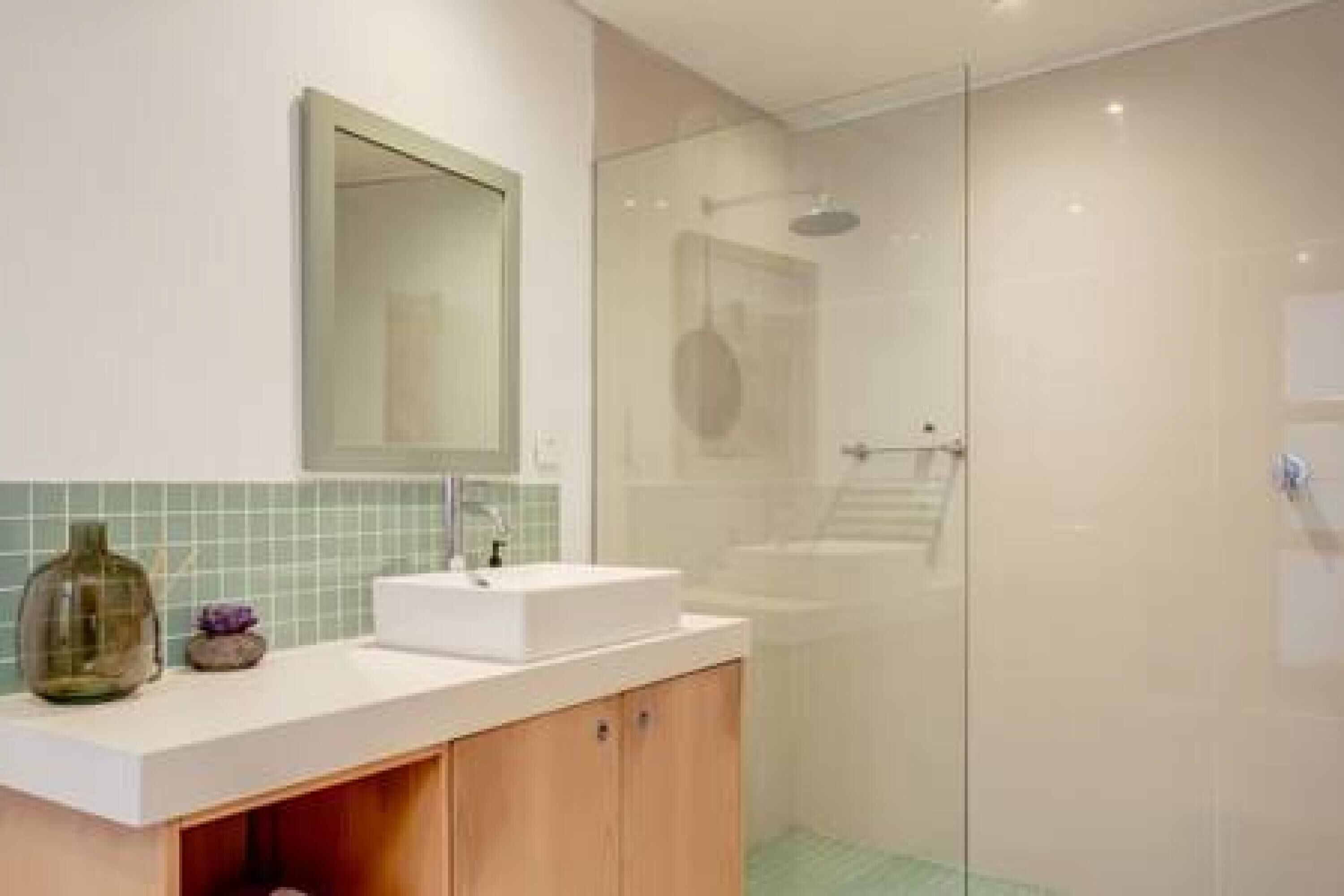 A modern bathroom with a glass shower enclosure, a white sink, and a mirror.