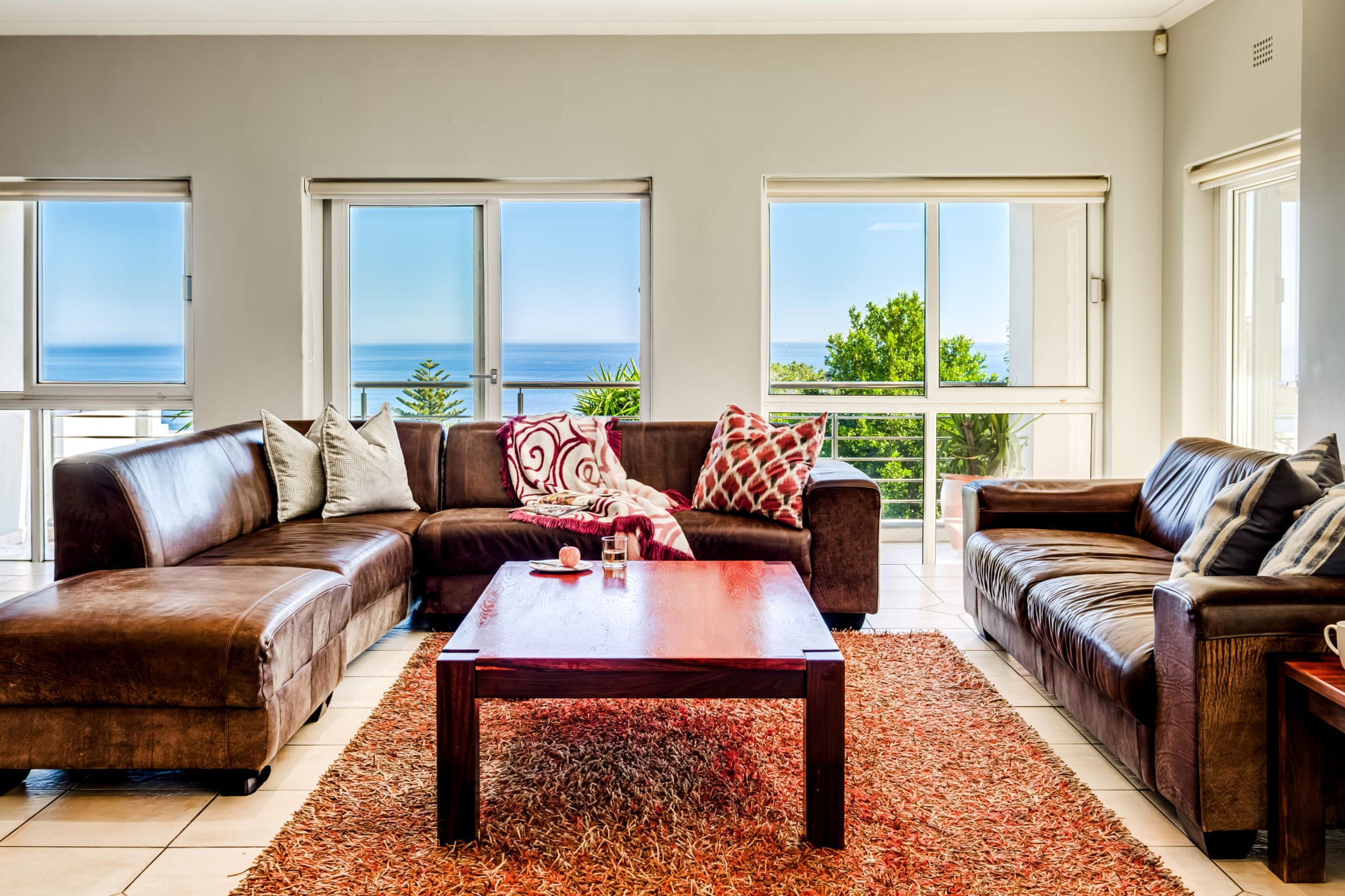 A living room with two brown leather sofas, a wooden coffee table, and a large window overlooking the sea.