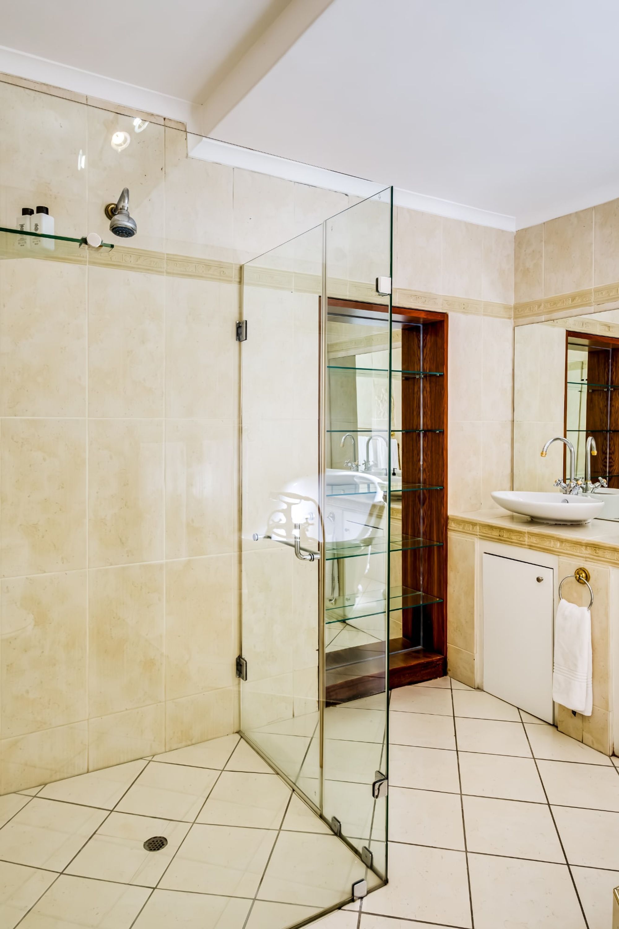A modern bathroom with a glass-enclosed shower, a sink with a mirror, and a tiled floor.