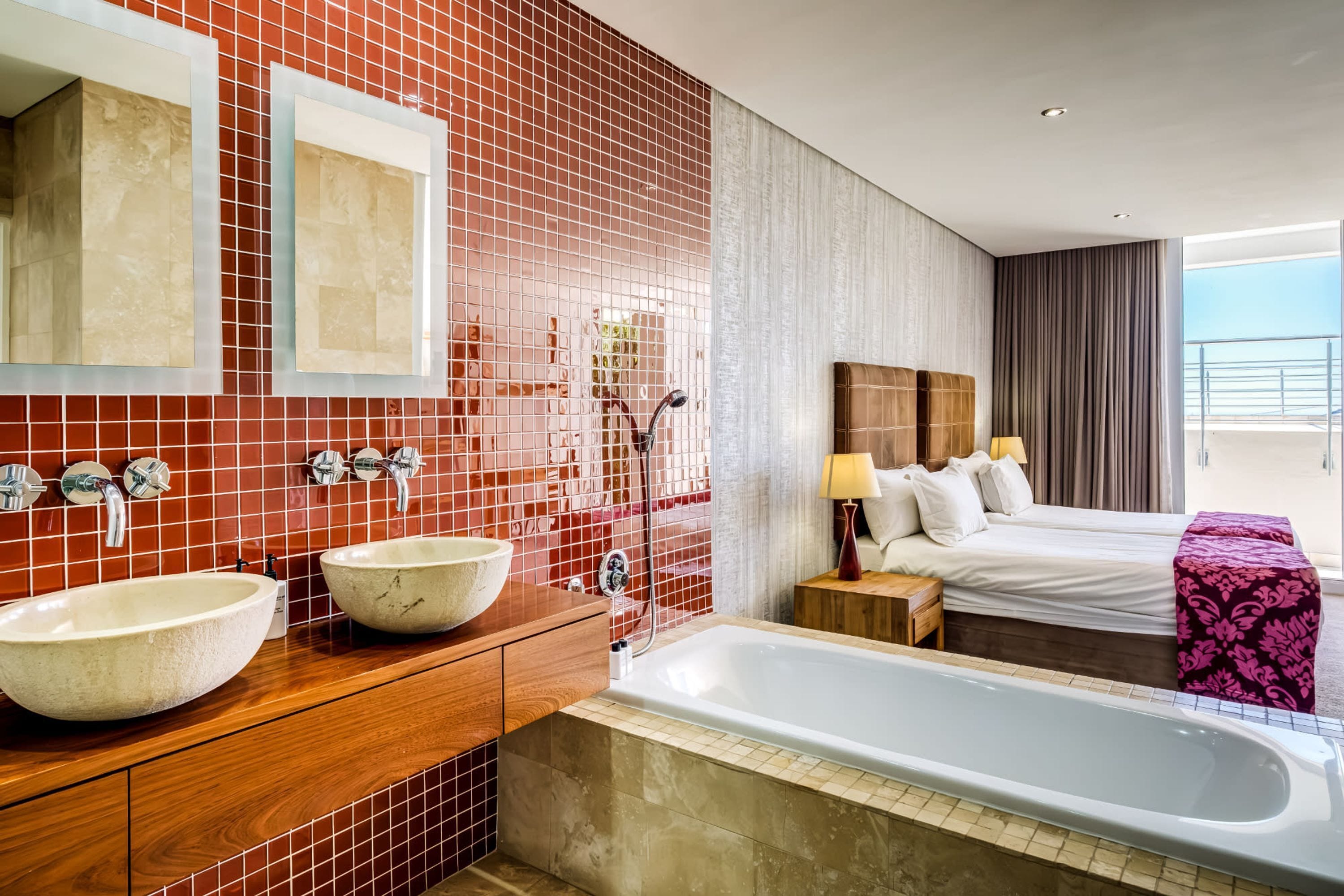 A modern bathroom with two large sinks, a bathtub, and a bed with a view.