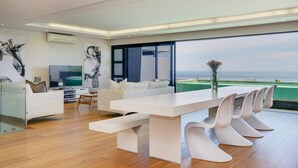 A modern dining area with a long table, white chairs, and a view of the ocean. - Spacious Holiday Apartment With Fantastic Views Deck Pool Malindi (Cape Town)