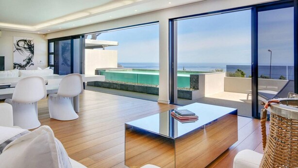 A modern living room with a glass coffee table, white furniture, and a view of the ocean. - Spacious Holiday Apartment With Fantastic Views Deck Pool Malindi (Cape Town)
