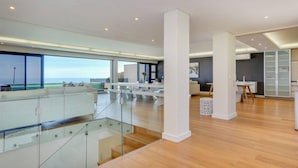 A spacious, modern interior with a glass balcony overlooking a scenic view, a central column, and a dining area with a view. - Spacious Holiday Apartment With Fantastic Views Deck Pool Malindi (Cape Town)