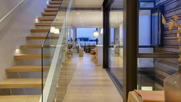 Un intérieur moderne avec un escalier en verre, un plancher en bois et une vue dégagée grâce à de grandes fenêtres.
