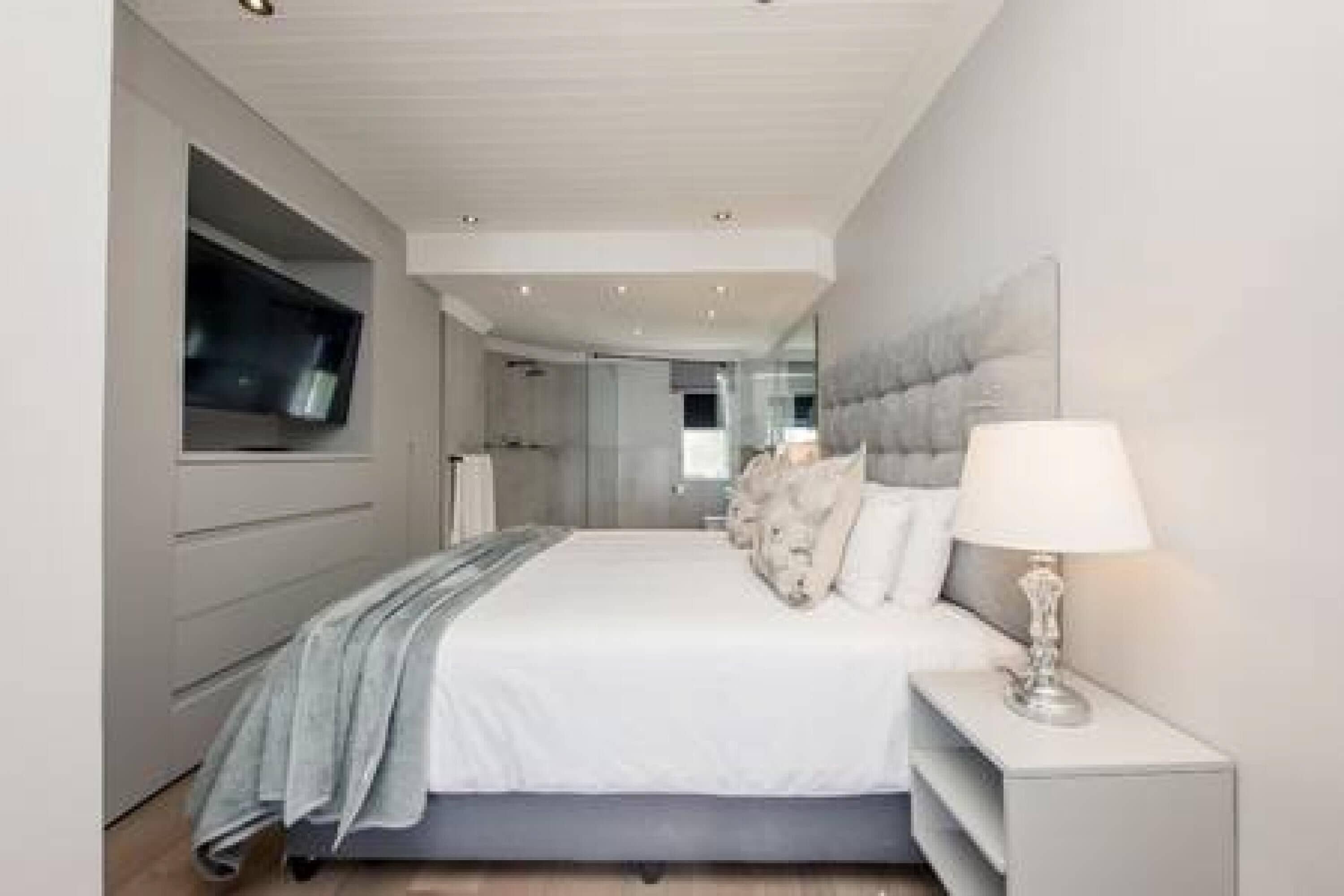 A modern bedroom with a large bed, a TV mounted on the wall, and a bedside table with a lamp.