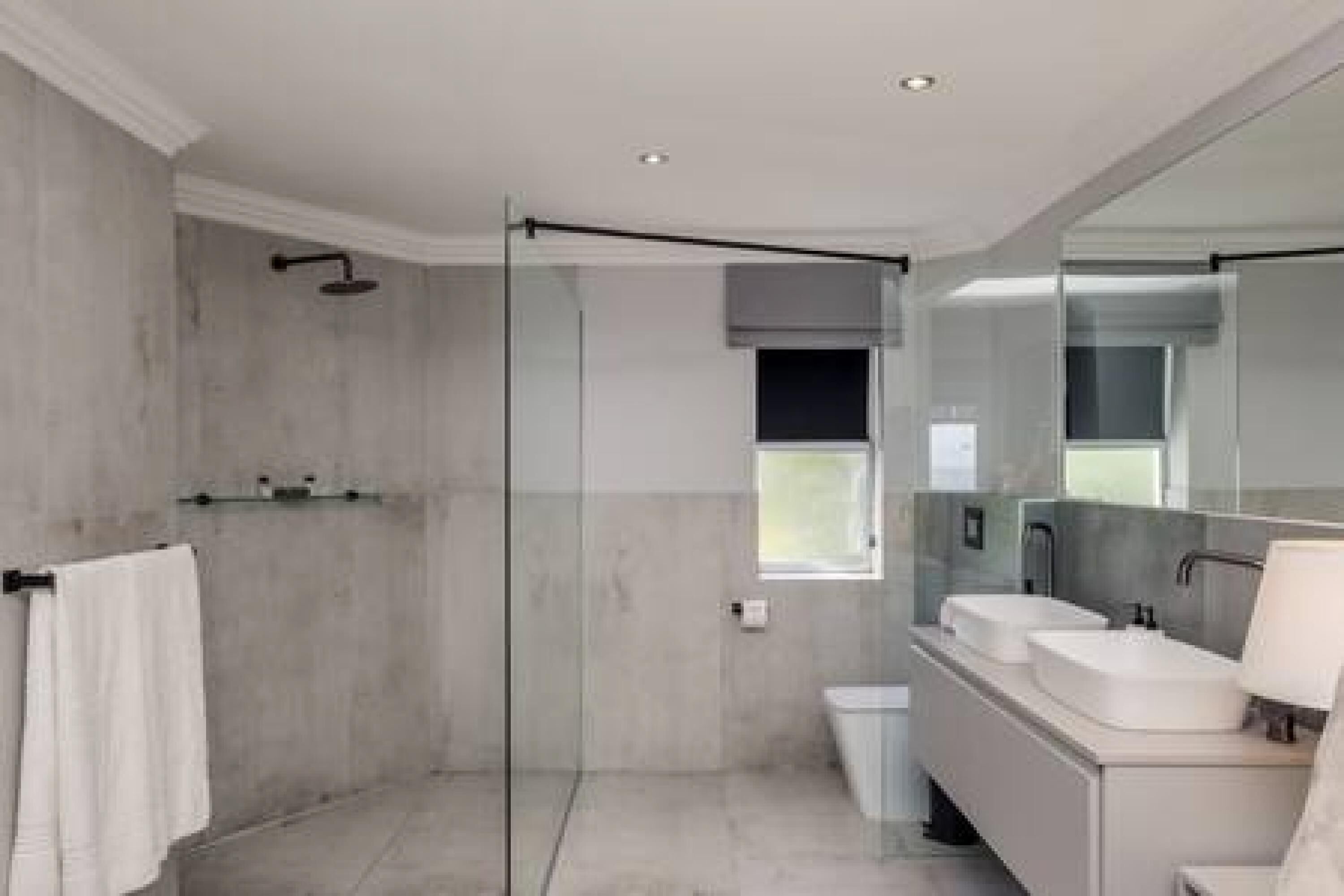 A modern bathroom with a glass shower enclosure, a large mirror, and a vanity with two sinks.