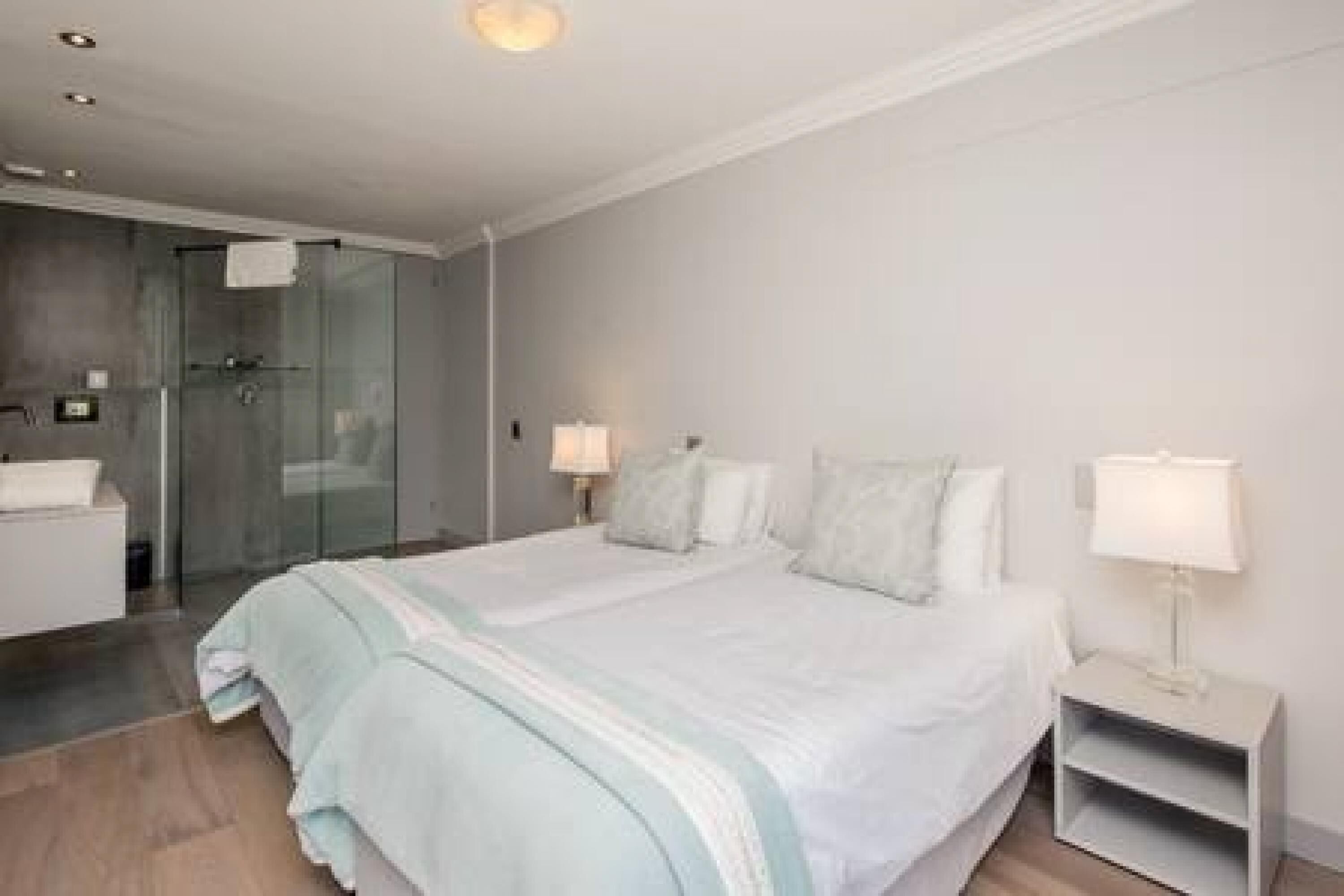 A modern hotel room with a large bed, bedside tables, a glass shower enclosure, and a white bathroom.