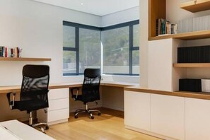 Ein modernes Büro mit Schreibtisch, zwei schwarzen Bürostühlen, einem Bücherregal und großen Fenstern.
