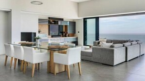 Un salon moderne avec une table à manger en verre, des chaises blanches et un canapé gris.