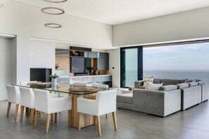 Una sala de estar moderna con una mesa de comedor de vidrio, sillas blancas y un sofá gris.