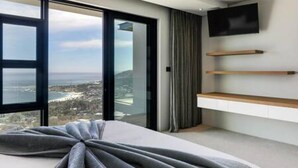 Une chambre d’hôtel moderne dotée d’une grande fenêtre donnant sur la ville, d’un téléviseur à écran plat fixé au mur et d’étagères en bois intégrées.
