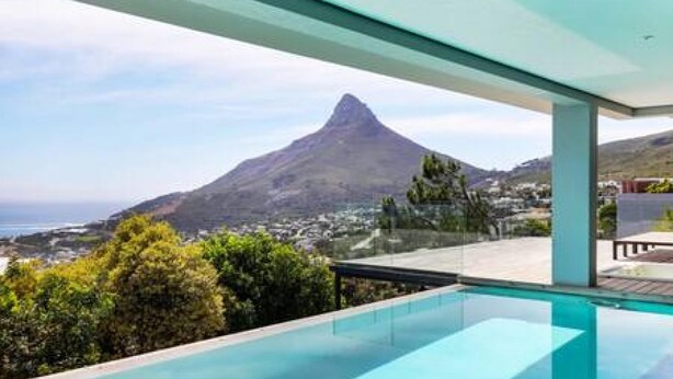 Une piscine à débordement moderne offrant une vue dégagée sur une montagne et l’océan.