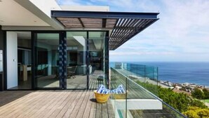 Un balcon moderne avec des garde-corps en verre, un plancher en bois et une vue sur l’océan.