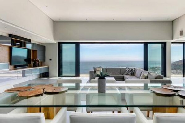 Ein modernes Wohnzimmer mit einem Glastisch, weißen Sofas und einem großen Fenster mit Blick auf den Ozean.