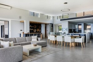 A spacious living area with a modern sofa set, a dining table with chairs, and a kitchen area with a bar.