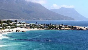 A coastal town with buildings along the beach, a mountain in the background, and clear blue waters.