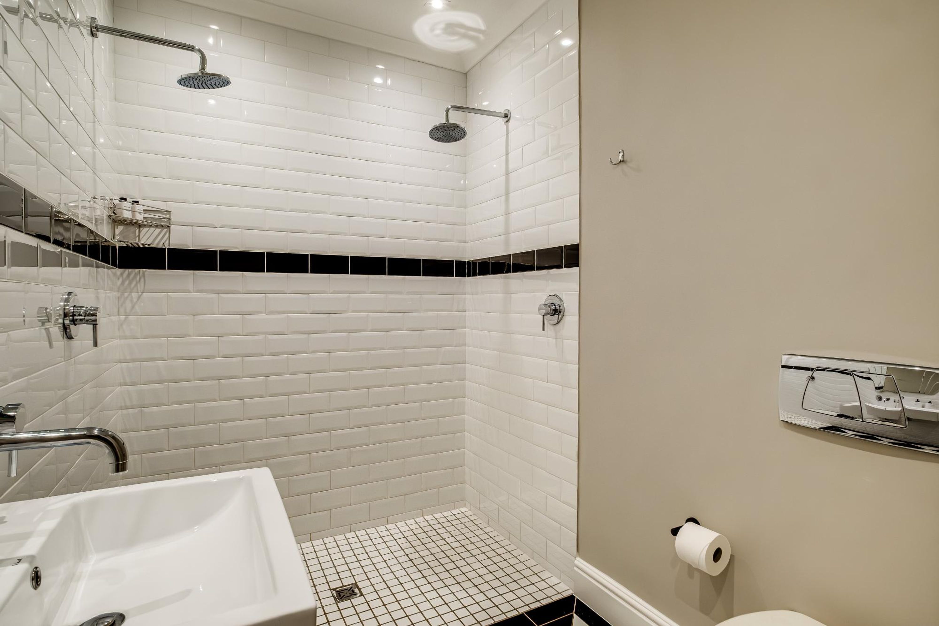 A modern bathroom with white subway tiles, a black-tiled accent wall, a shower with a handheld showerhead, a sink, and a toilet.