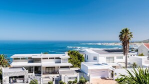 A coastal residential area with modern white houses, a palm tree, and a view of the ocean. - Spacious Holiday Villa w Private Pool Garden Serein (Cape Town)