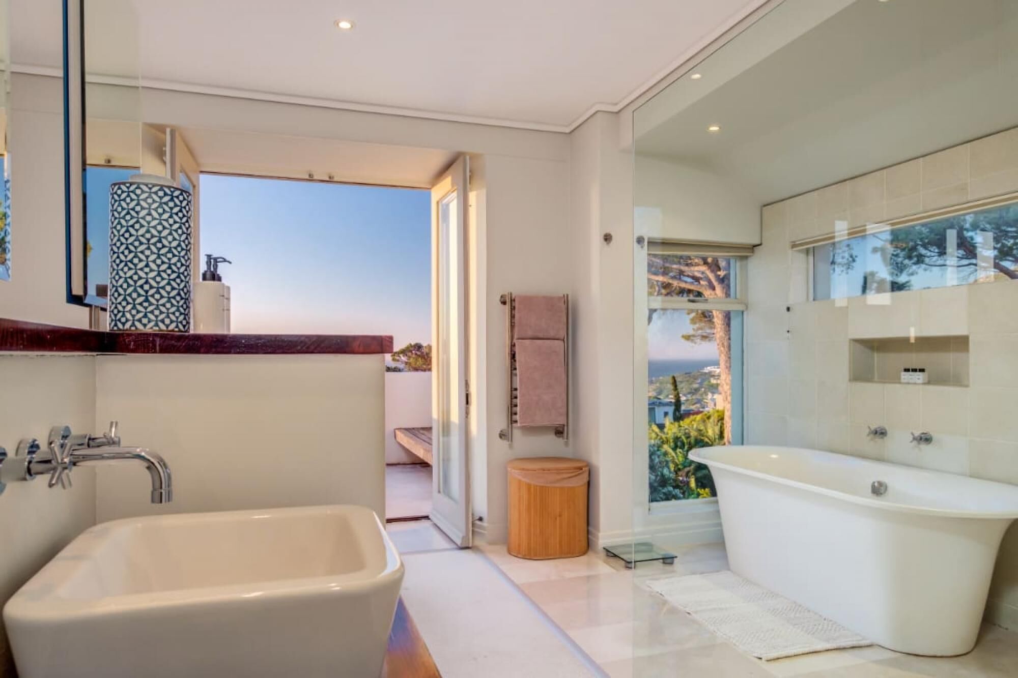 A modern bathroom with a large bathtub, a separate shower area, and a glass-enclosed window offering a scenic view.