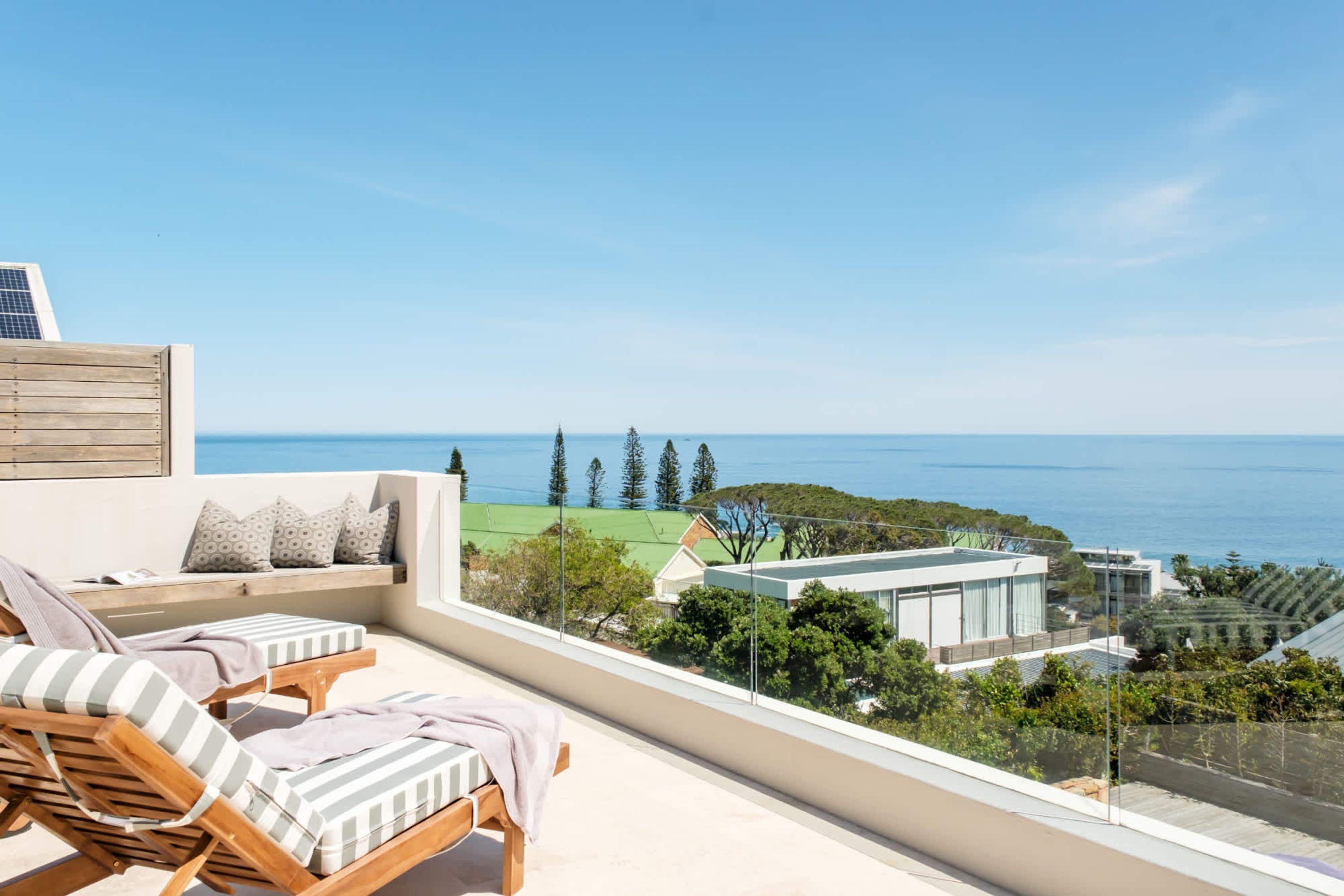 A rooftop terrace with wooden lounge chairs and a view of the sea and greenery.