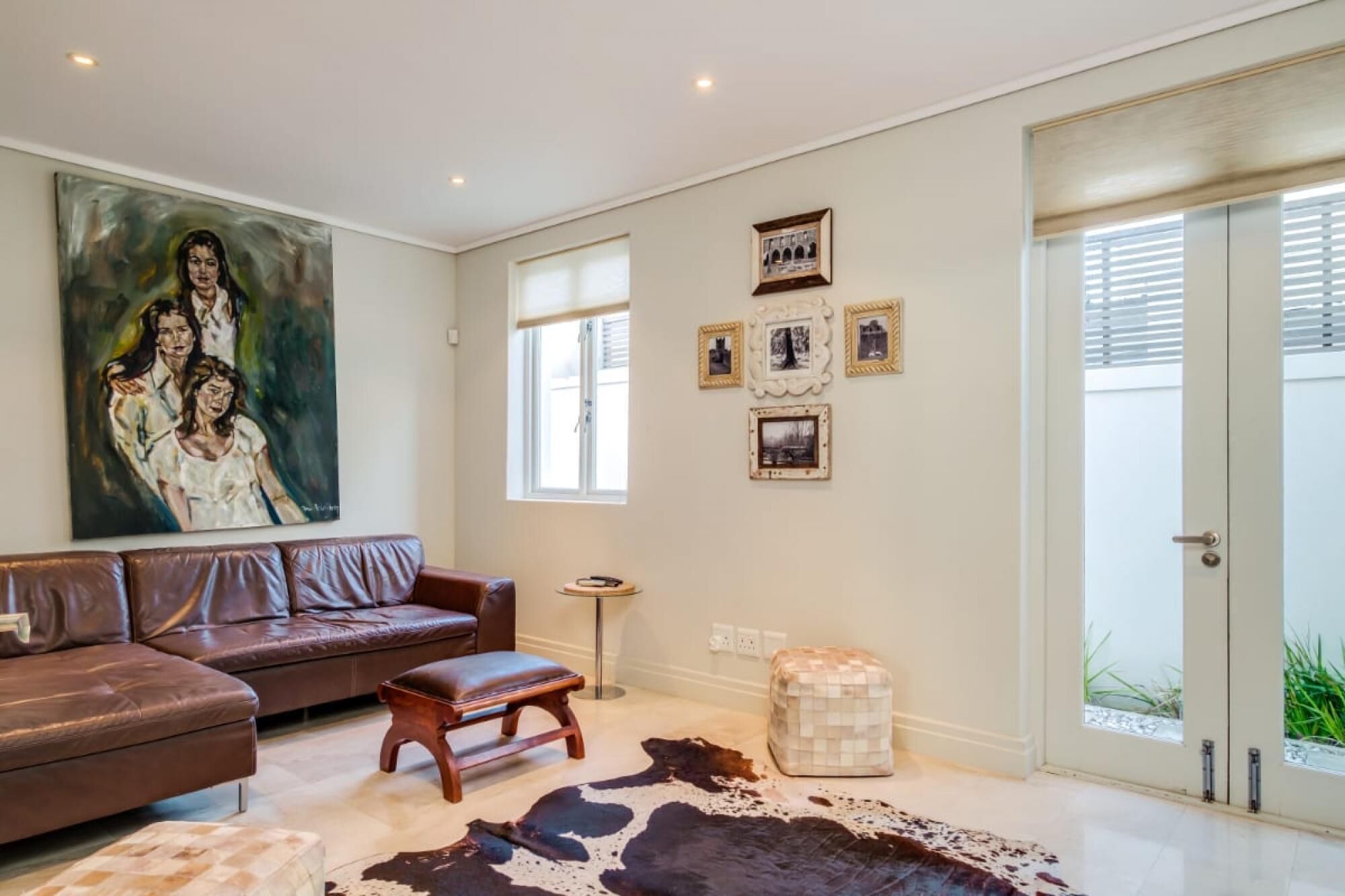 A living room with a brown leather sofa, a wooden coffee table, a large abstract painting, and a cowhide rug.