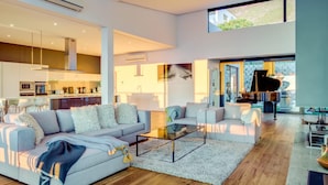 A spacious living area with a large sofa, a glass coffee table, and a piano in the background. - Incredible Villa w Lap Pool Ocean Views Casa Di Sorrento (Cape Town)