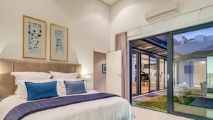 A modern bedroom with a large bed, a glass door leading to a patio, and two framed artworks on the wall. - Incredible Villa w Lap Pool Ocean Views Casa Di Sorrento (Cape Town)
