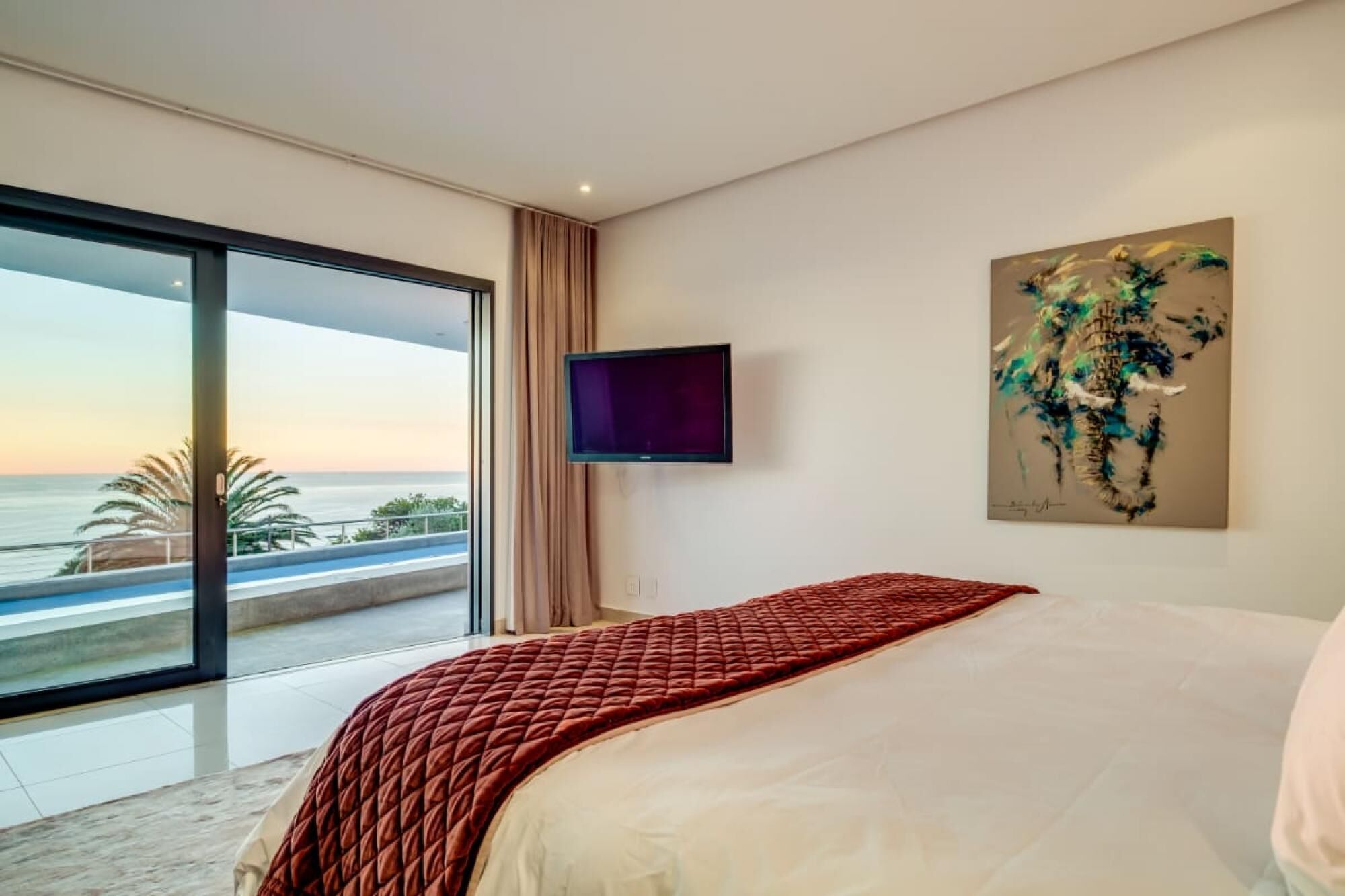 Een slaapkamer met een groot bed, een aan de muur bevestigde televisie en een schilderij.