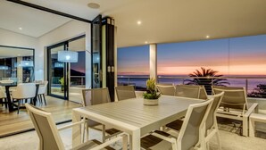 A dining area with a table and chairs, a potted plant, and a view of the sunset over the ocean. - Incredible Villa w Lap Pool Ocean Views Casa Di Sorrento (Cape Town)