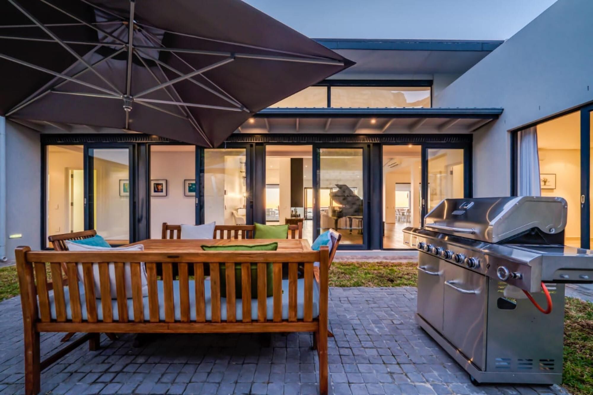 An outdoor patio with a wooden table and bench, a grill, and a large umbrella.