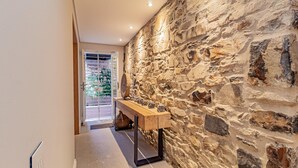 A hallway with a stone wall, a wooden bench, and a door leading to a balcony with plants. - Stylish Apartment With Rooftop Deck Pool 53 Napier (Cape Town)