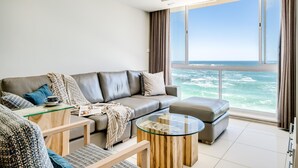 A modern living room with a large window offering a view of the ocean. - Clifton Apartment w Direct Beach Access Marella (Cape Town)