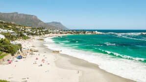 A coastal beach with clear turquoise waters, a sandy shore, and a mountainous backdrop. - Clifton Apartment w Direct Beach Access Marella (Cape Town)