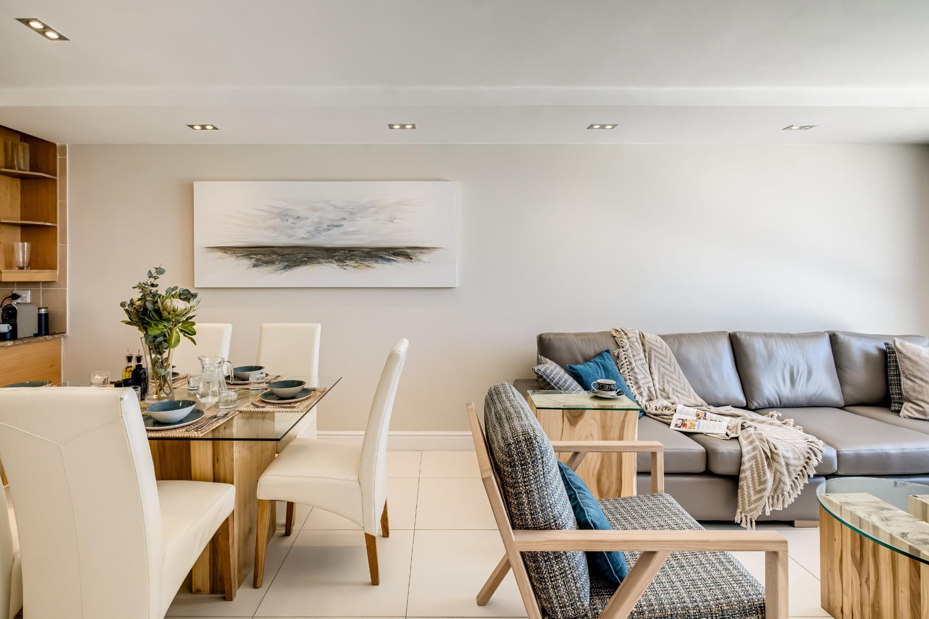 Een moderne woonkamer met een glazen eettafel, witte stoelen, een grijze bank en een salontafel.