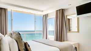 A bedroom with a large bed, a TV mounted on the wall, and a view of the ocean through the windows. - Clifton Apartment w Direct Beach Access Marella (Cape Town)