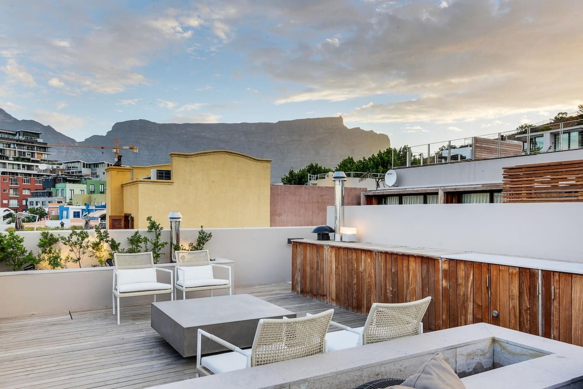 A rooftop terrace with outdoor seating, a pool, and views of a cityscape and mountains.