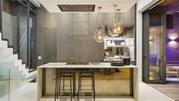 Une cuisine moderne dotée d’un îlot central, de tabourets de bar, de luminaires suspendus et d’une cuisinière intégrée.