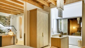 Une chambre à coucher moderne avec un grand lit, des poutres en bois, une armoire et une salle de bain visible à travers une porte ouverte.