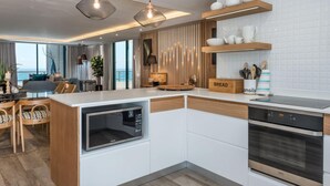 A modern kitchen with a built-in oven, microwave, and a dining area with a view of the sea. - Stylish Secure Camps Bay Holiday Apartment 9 Nautica (Cape Town)