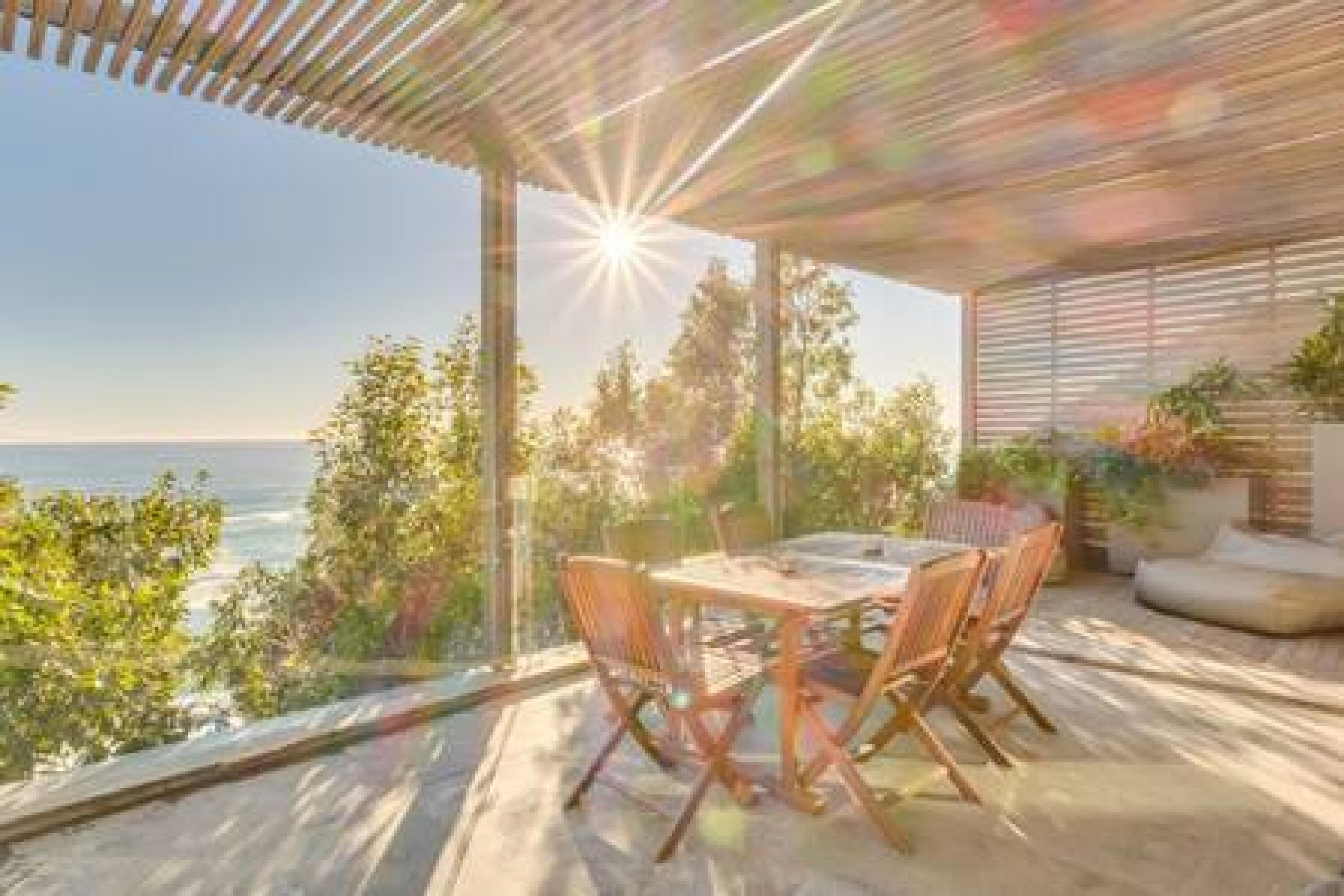 A patio with a table and chairs, overlooking a scenic view of the ocean and trees.