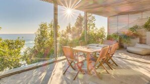 A patio with a table and chairs, overlooking a scenic view of the ocean and trees. - Unique Camps Bay Apartment w Private Pool Coral Sea (Cape Town)