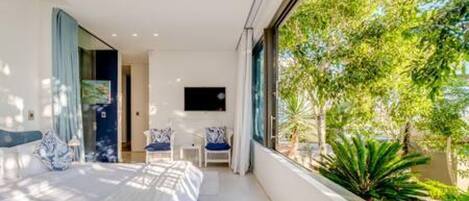 A modern bedroom with a large bed, a TV, and a view of greenery outside.