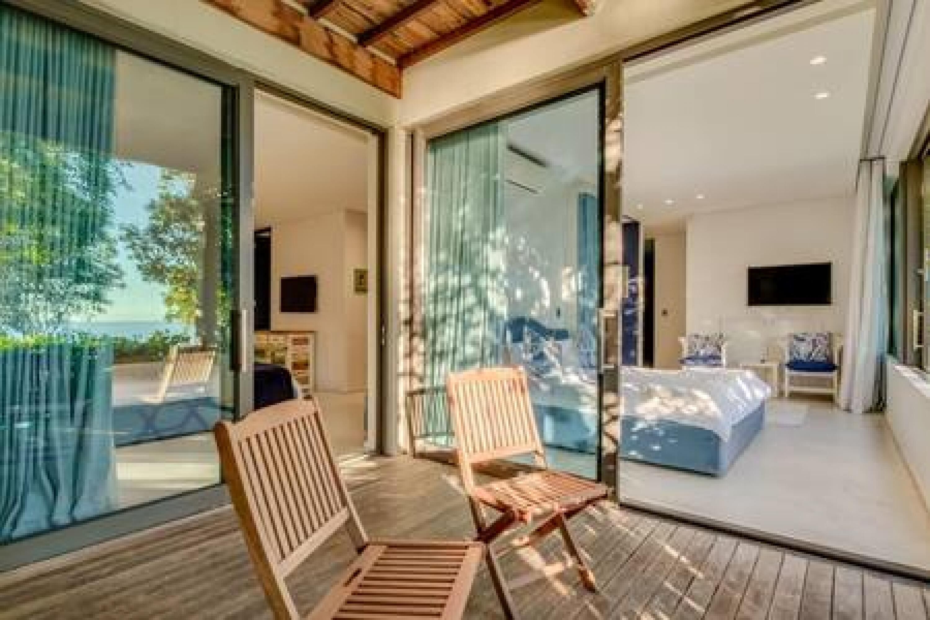 A modern room with a large sliding glass door leading to a balcony, a bed, a TV, and a seating area with chairs.