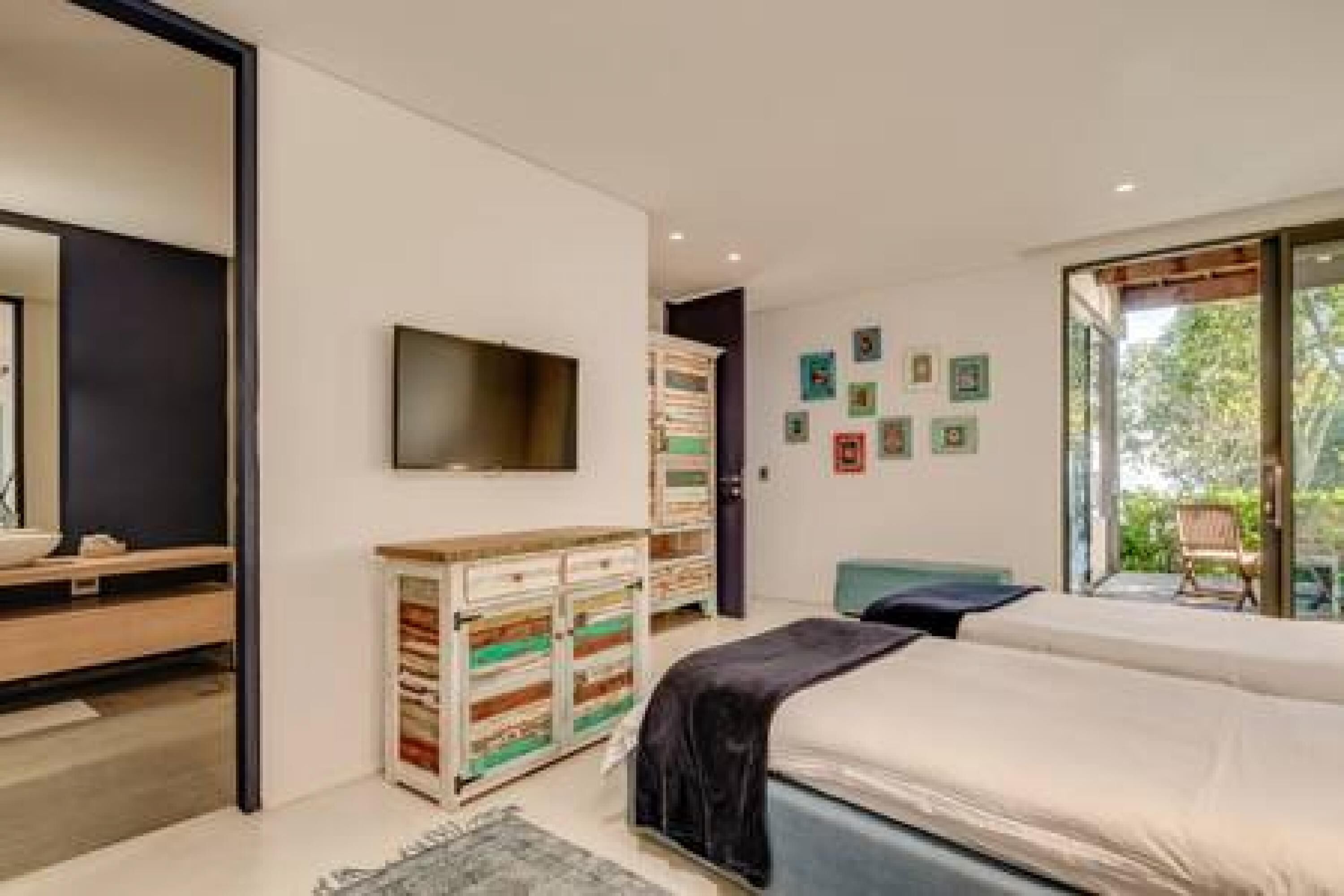 A modern bedroom with a bed, a TV, a dresser, and a view of the outdoors.