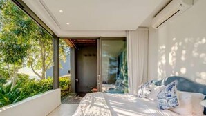A modern bedroom with a large bed, a glass door leading to a balcony, and a view of greenery outside. - Unique Camps Bay Apartment w Private Pool Coral Sea (Cape Town)