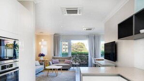 A modern kitchen with built-in appliances, a dining area with a sofa and table, and a TV mounted on the wall. - Stylish 2 Bedroom Apartment in Camps Bay Asilvertide (Cape Town)