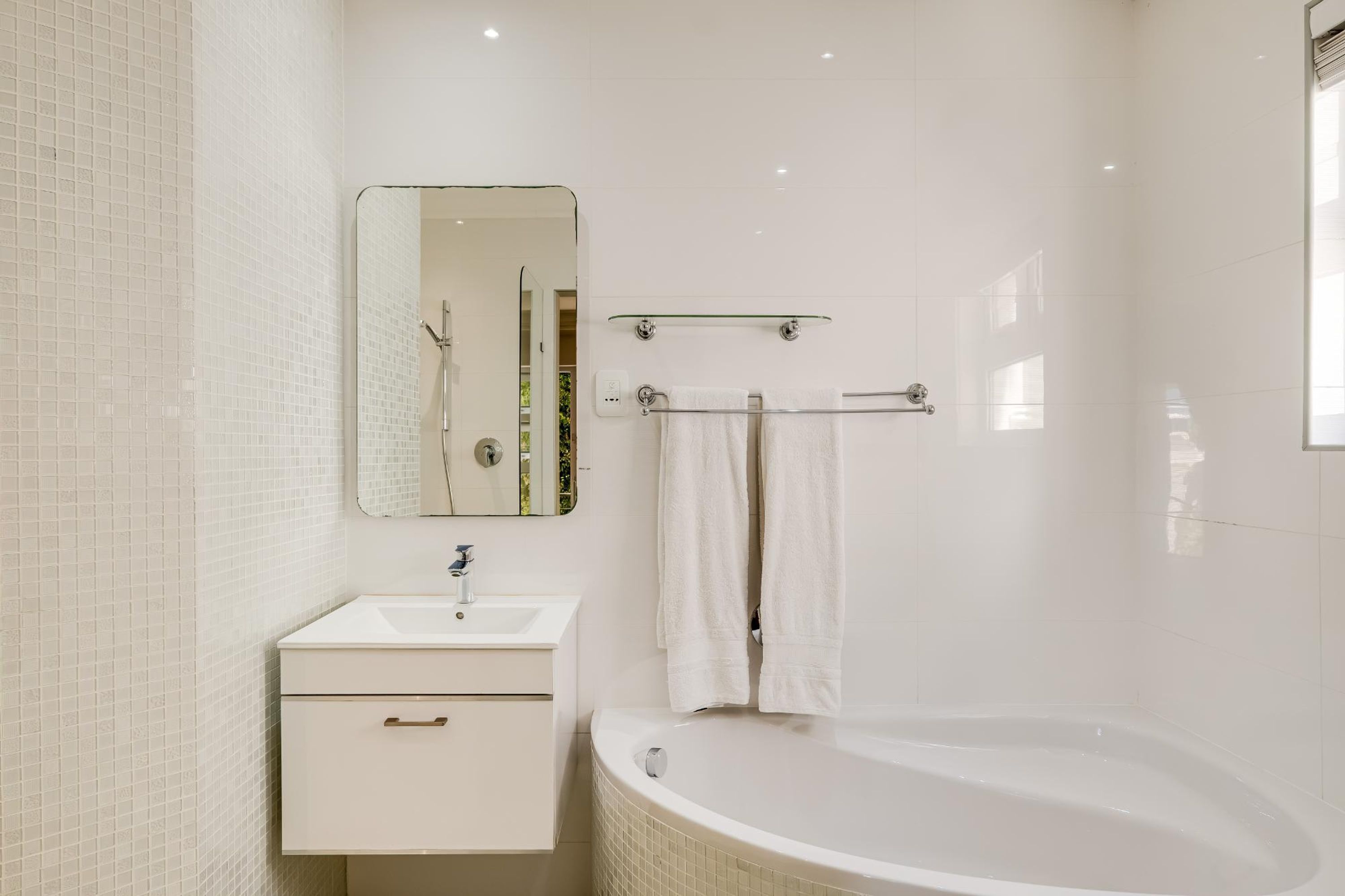 A bathroom with a white sink, mirror, and bathtub.