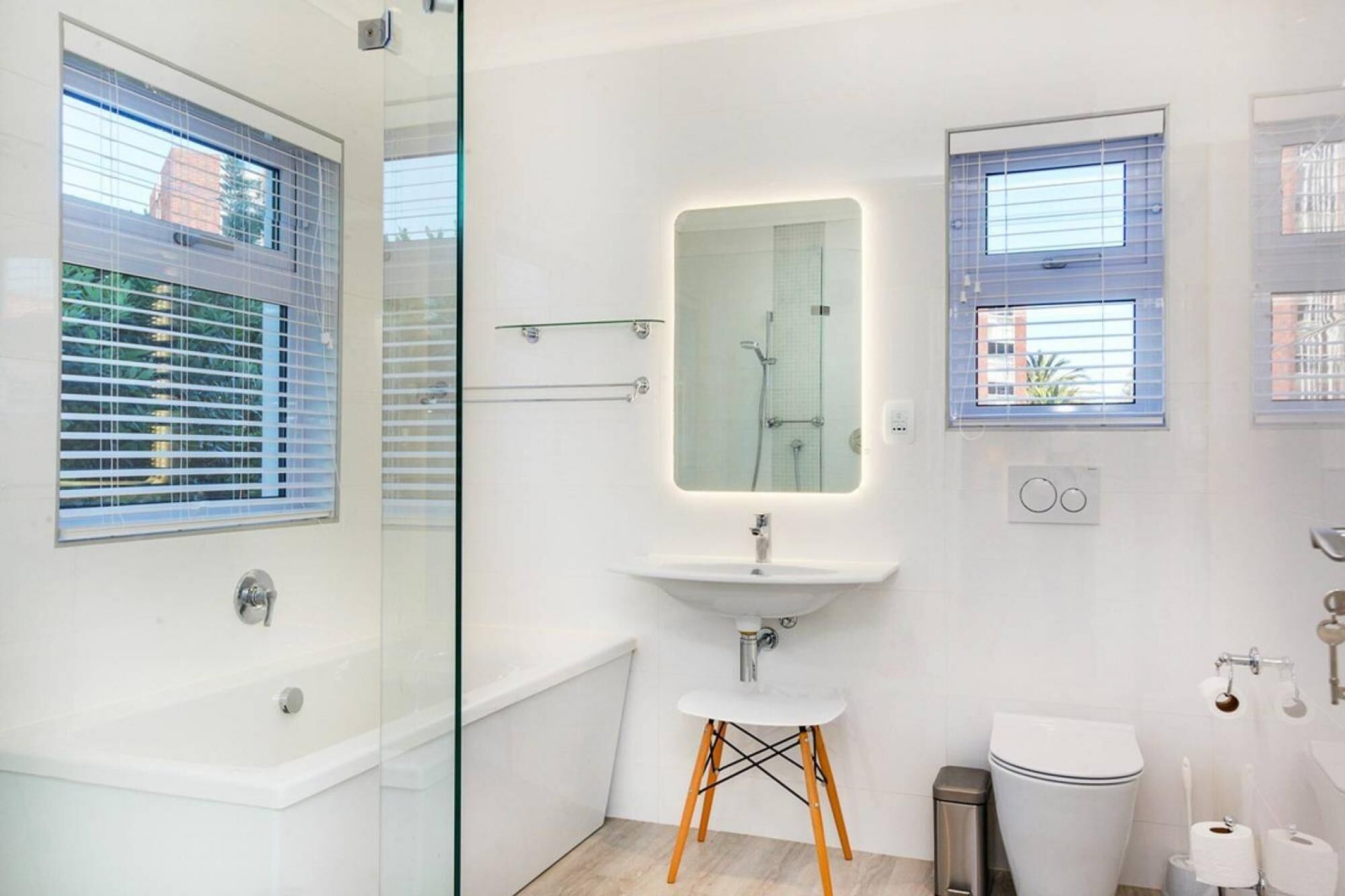 Een moderne badkamer met een glazen douchecabine, een witte wastafel met spiegel en een toilet.